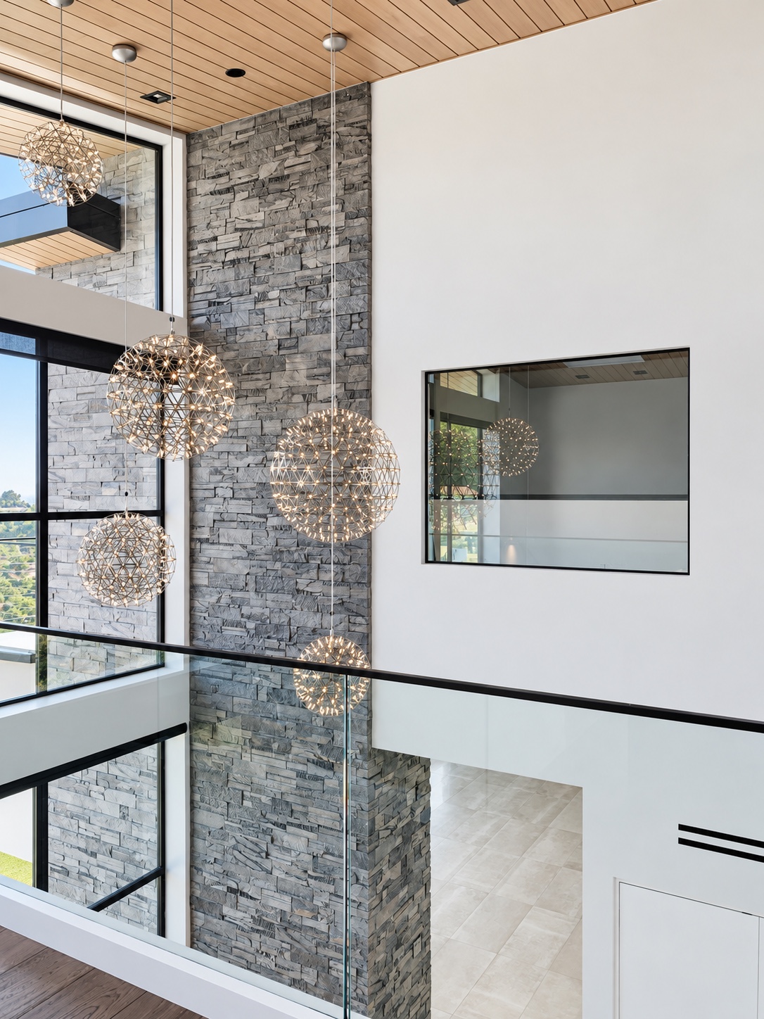 Pendant lights, stone wall, and glass railing in a double-height interior — Diamond Bar, CA